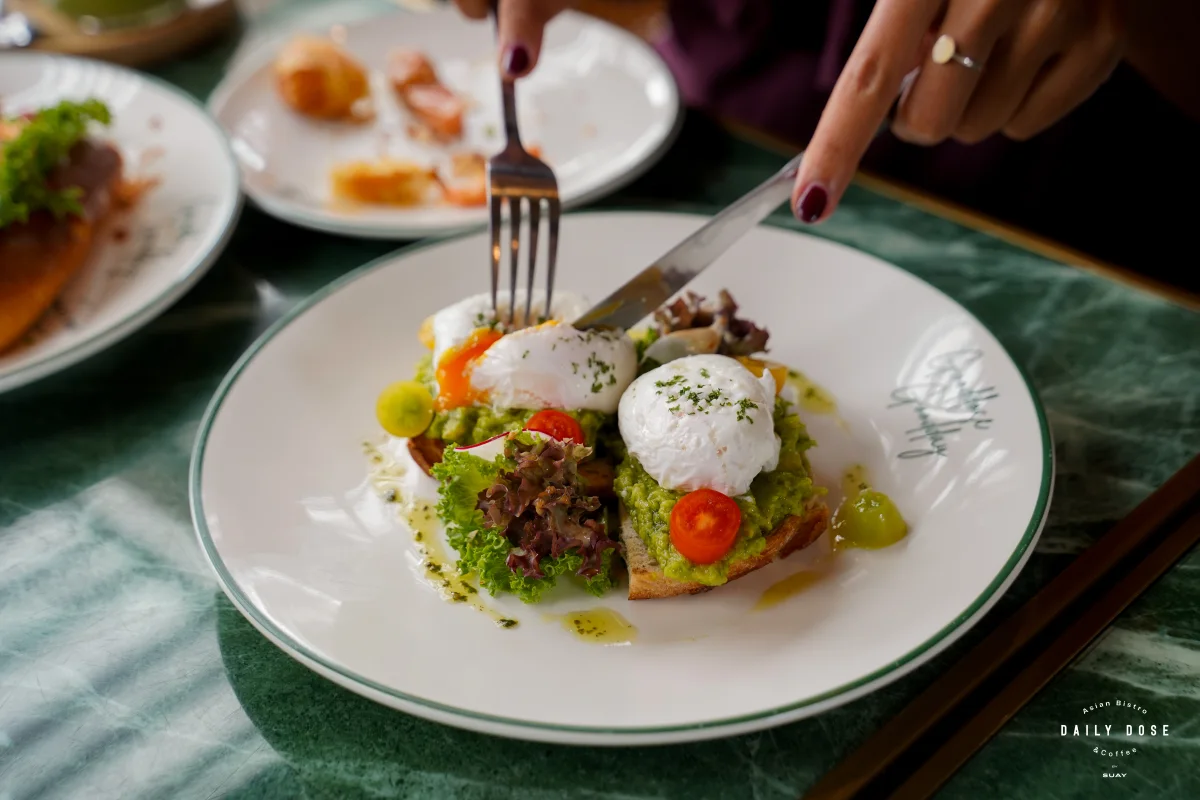 Eggs Benedict on avocado toast being cut with a knife and fork