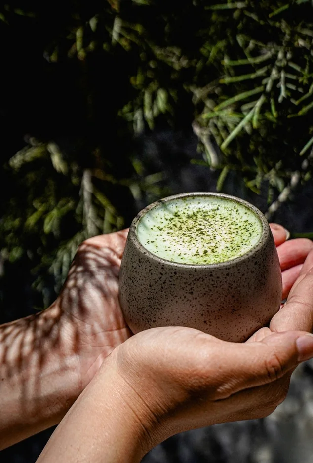 Hands holding a ceramic cup of matcha latte